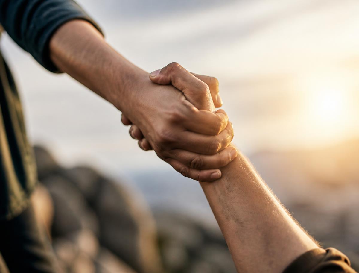 Two people clasping hands as one helps pull the other up